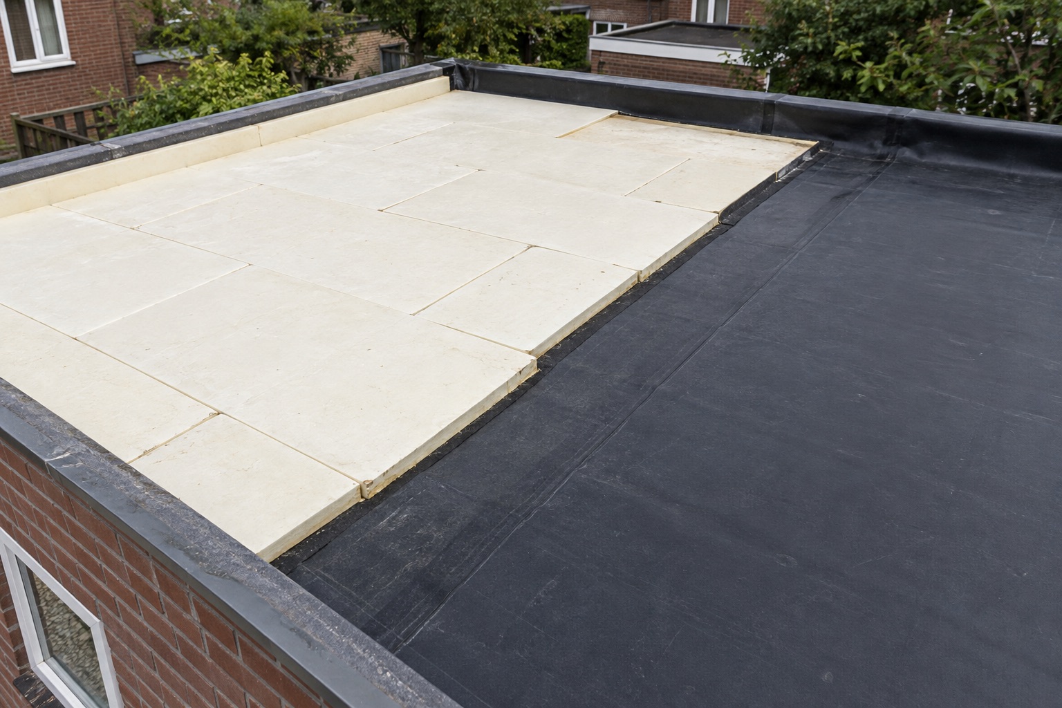Isolatieplaten naast de al aangebrachte zwarte dakbedekking tijdens een dakrenovatie
