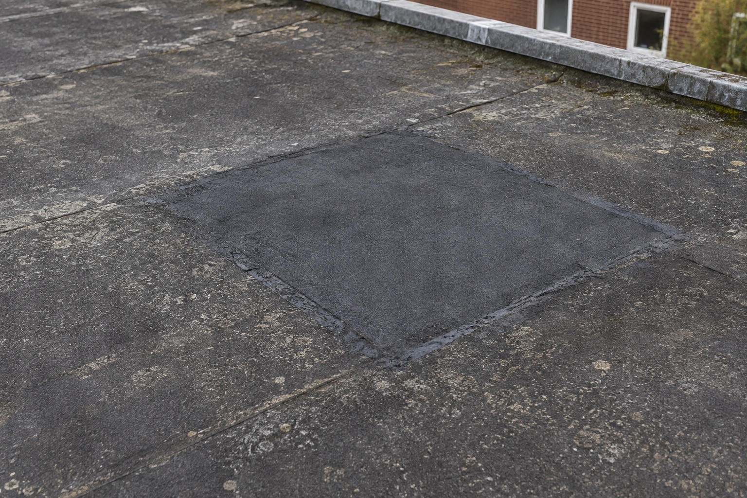 Plaatselijke reparatie op een verder verweerd zwart plat dak