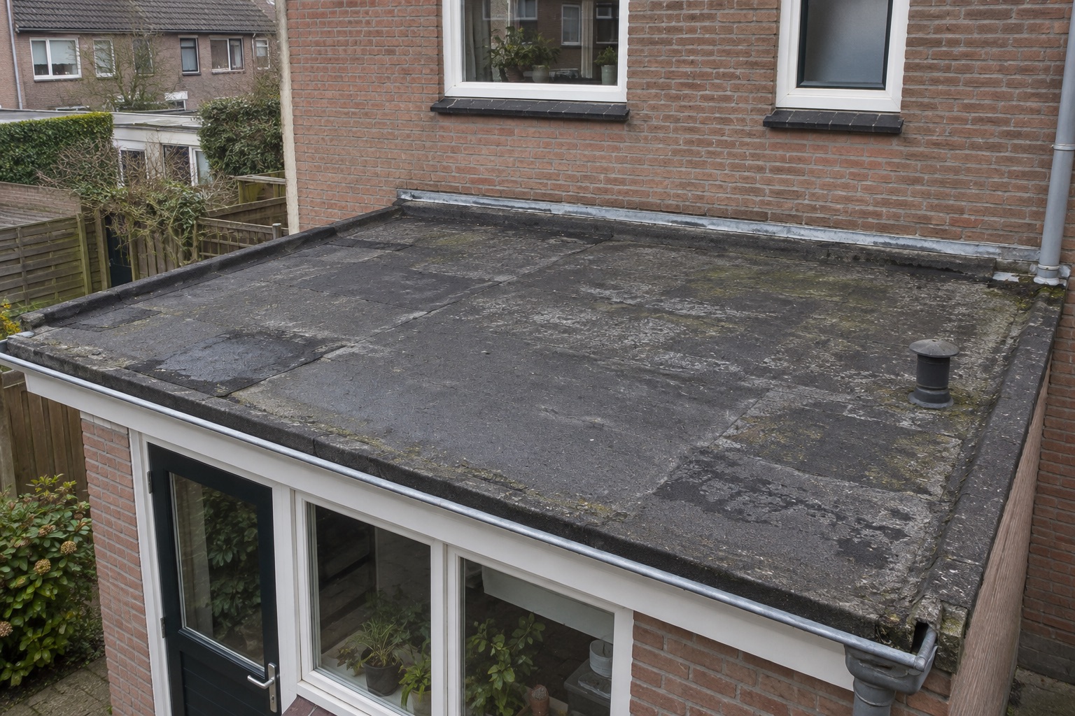 Verouderde bitumen dakbedekking met zichtbare eerdere reparaties